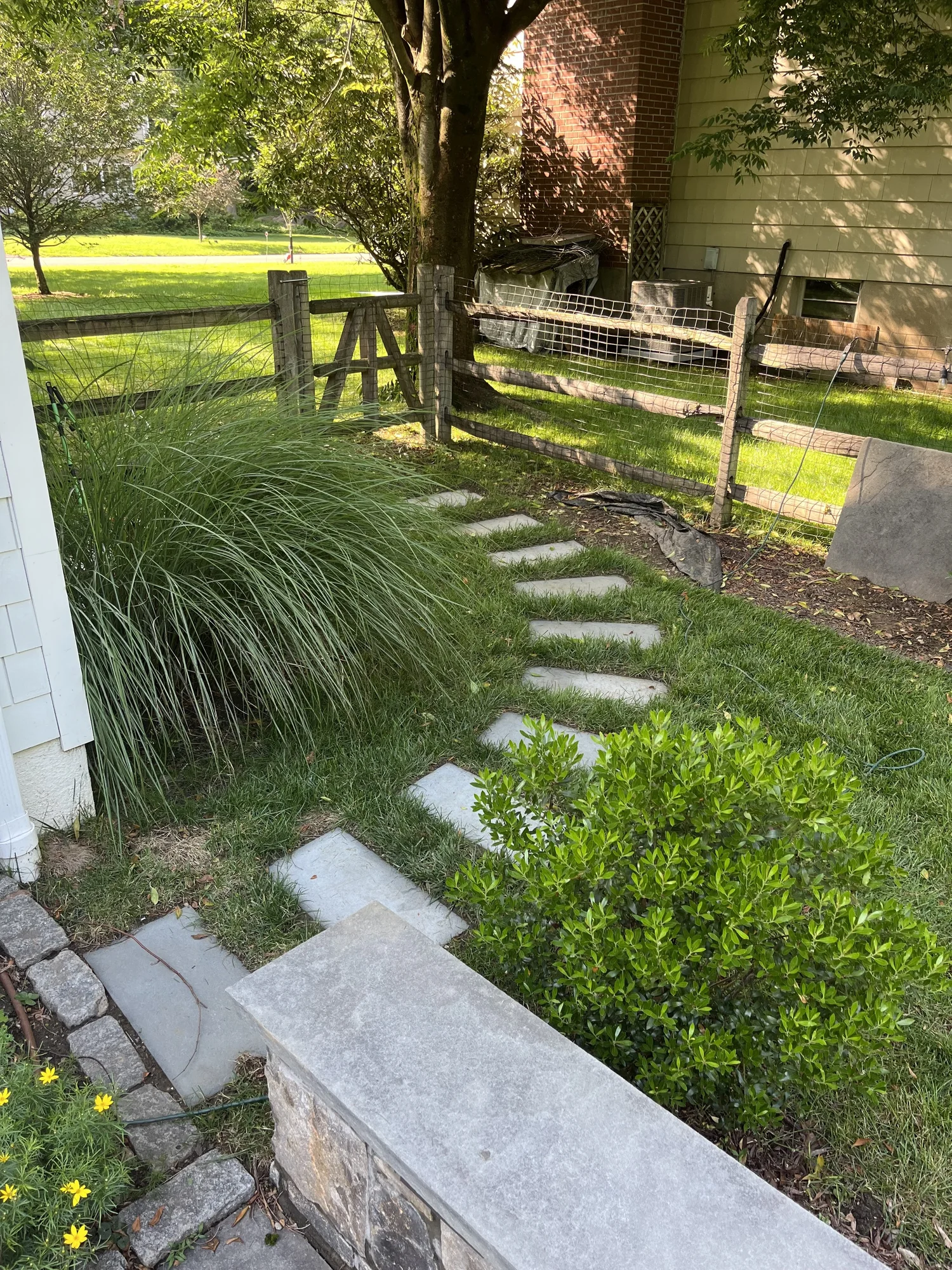 Stone pathway through a garden bed beside a wooden fence